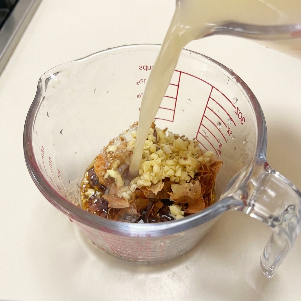 Caldo de cerdo caliente y opaco vertiéndose desde una jarra en una taza medidora con miso, ajo, bonito y condimentos.