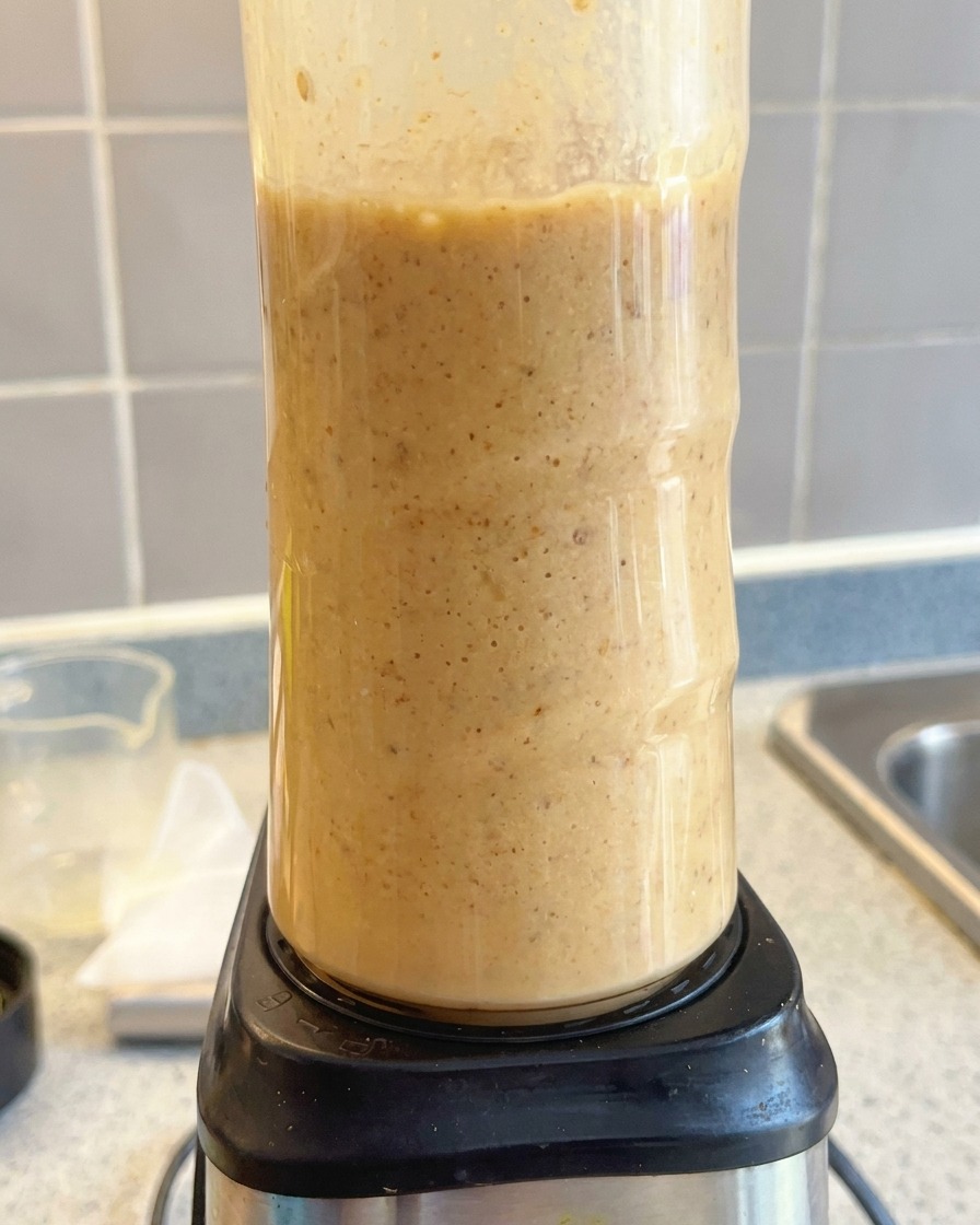 Un procesador de alimentos triturando una base de sopa tonkotsu de color marrón claro hasta que está cremosa.