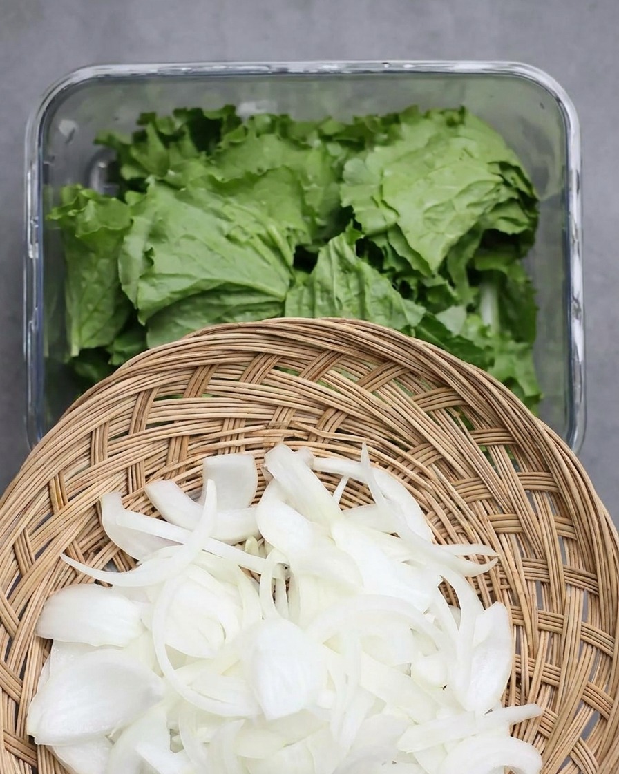 Una cesta de mimbre con cebollas blancas cortadas en rodajas finas sostenida sobre un recipiente con lechuga fresca.