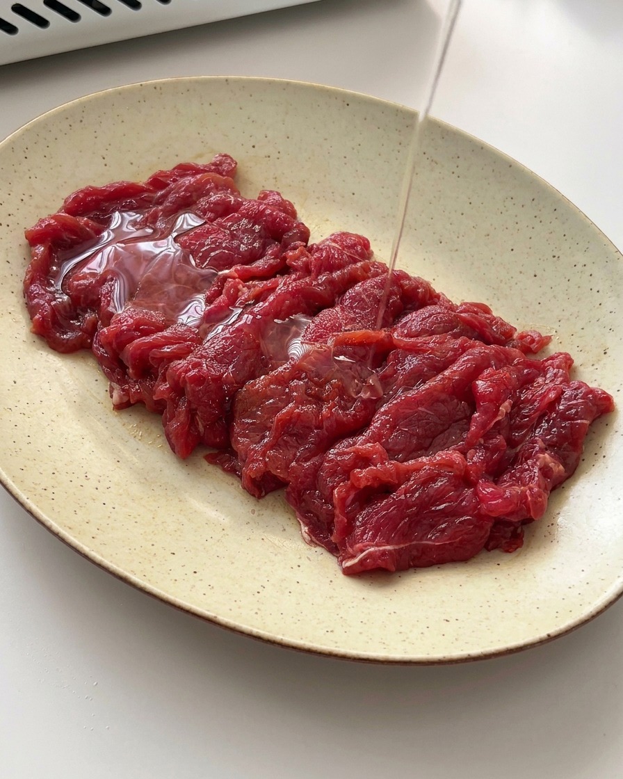 Un hilo de aceite vegetal vertiéndose sobre la ternera marinada en un plato.
