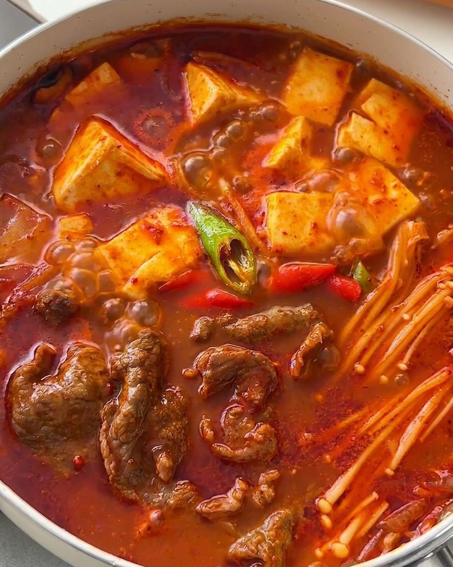 Estofado coreano de ternera y tofu burbujeante decorado con rodajas diagonales de chiles verdes y rojos.