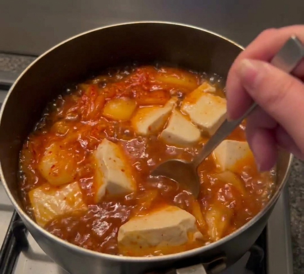 Una cuchara removiendo la sopa de color rojo anaranjado para mezclar bien la pasta de chile y la salsa de soja.