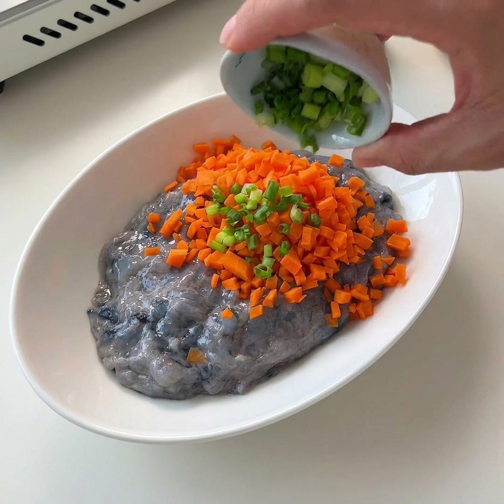 Zanahorias naranjas finamente picadas vertiéndose en un bol blanco con pasta de gambas cruda.