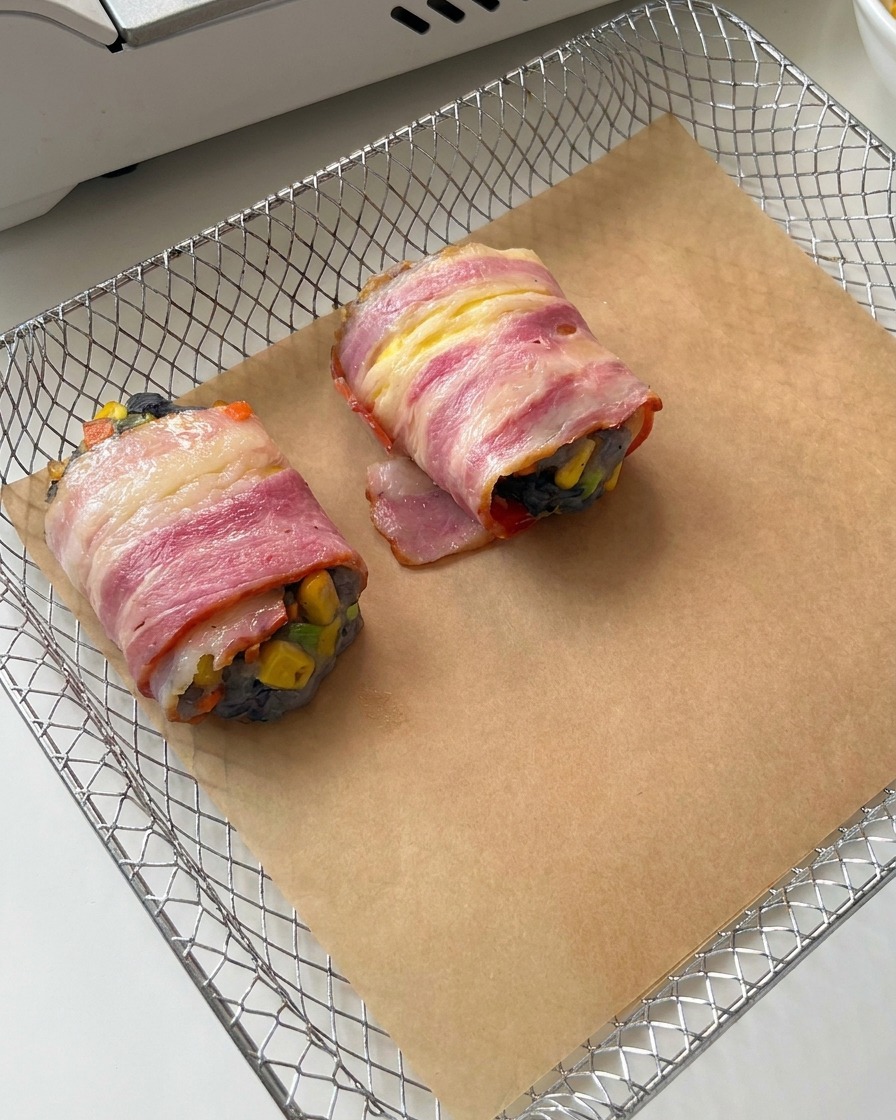 Rollitos de bacon y gambas crudos sobre papel vegetal dentro del cestillo de una freidora de aire.