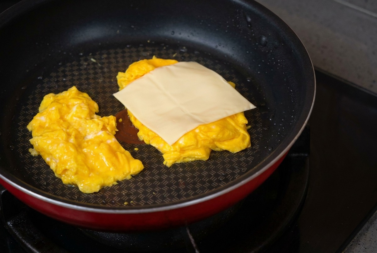 Una sartén antiadherente con dos montones de huevos revueltos y una rebanada de queso colocándose encima.