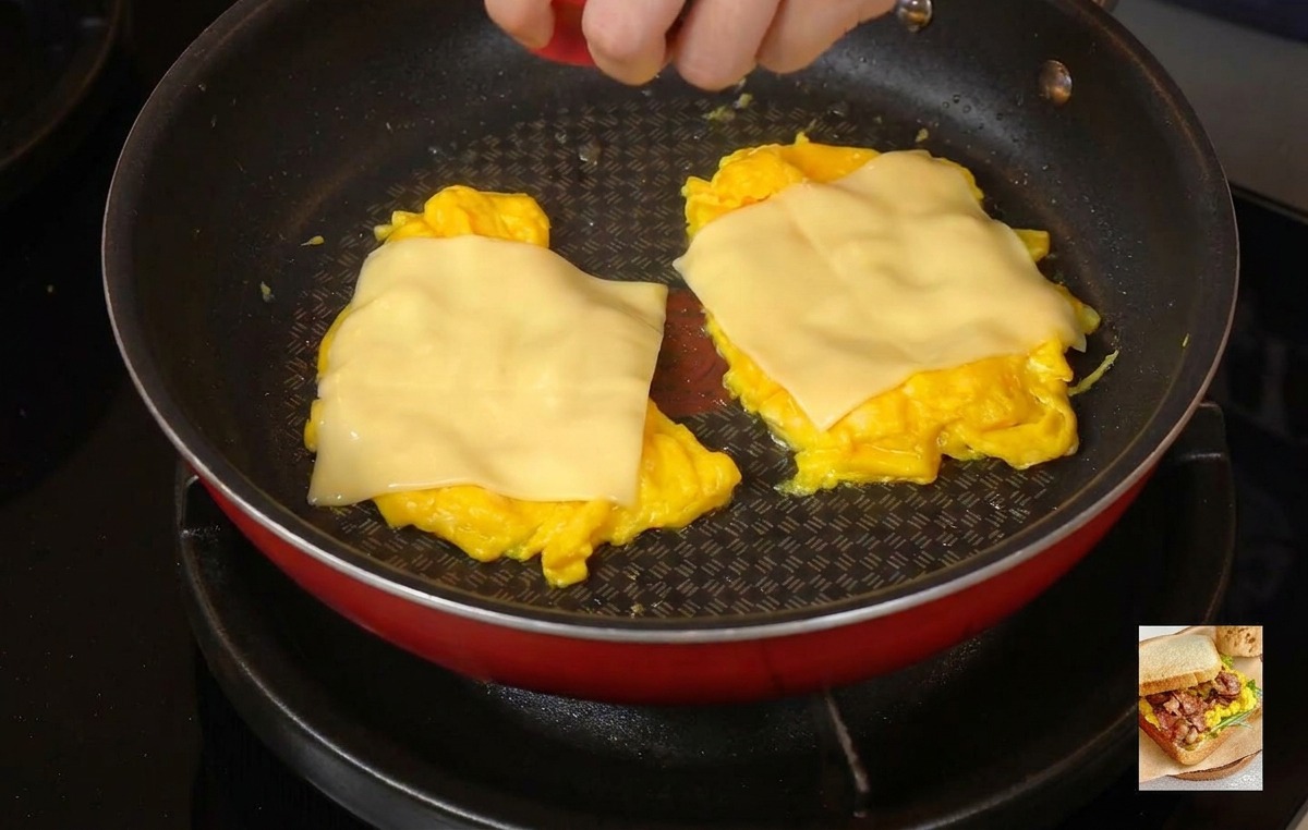 Una persona colocando una tapa roja sobre una sartén para atrapar el vapor y fundir el queso sobre los huevos.