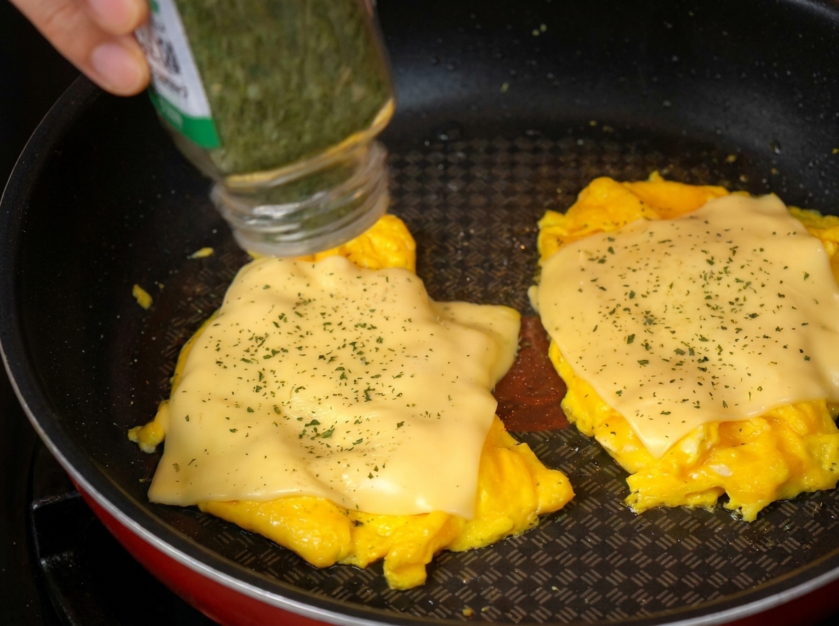 Primer plano de perejil seco espolvoreándose sobre los huevos revueltos con queso en la sartén.
