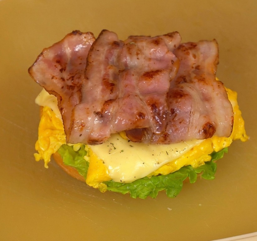 Hamburguesa abierta sobre una tabla mostrando capas de lechuga, tomate, huevo con queso y tocino crujiente.