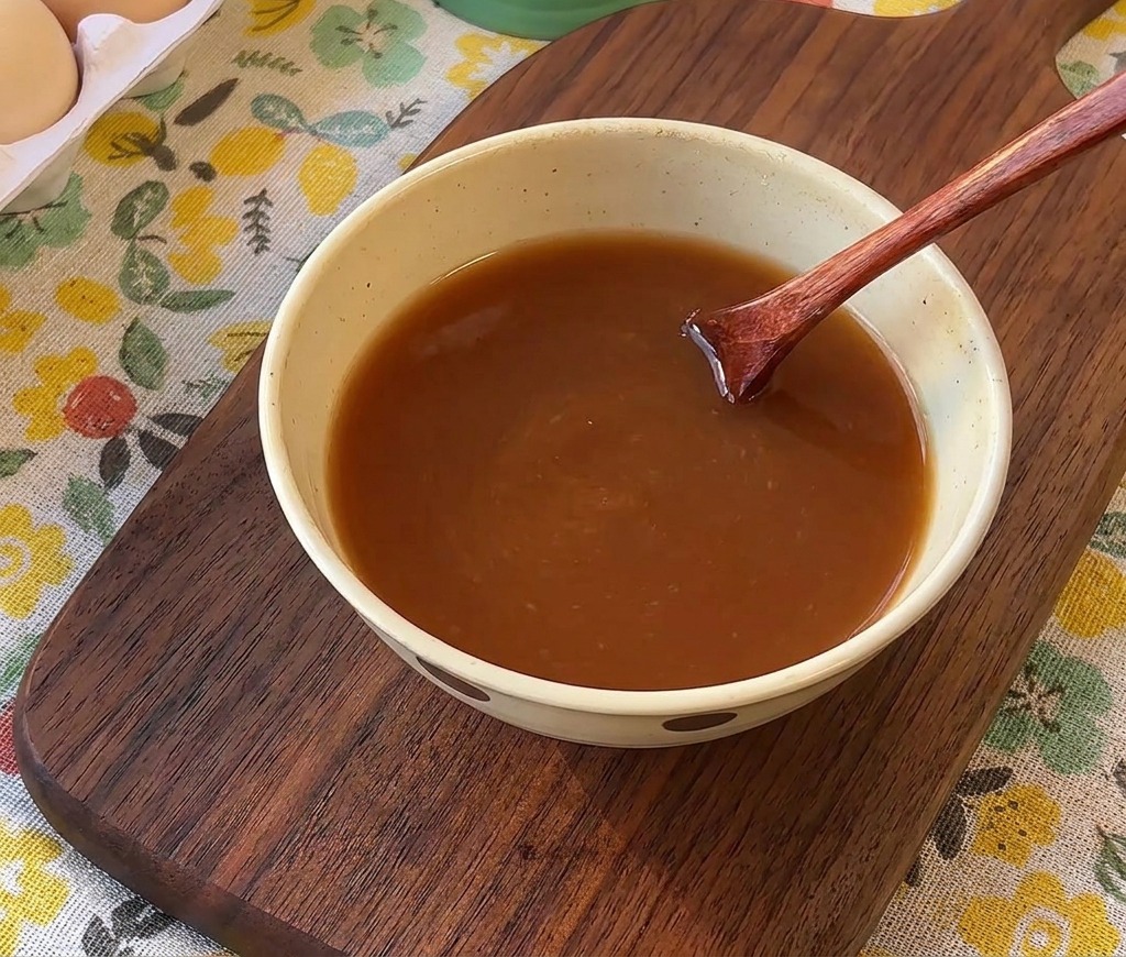 Cuchara de madera removiendo una salsa de color marrón en un bol de cerámica.