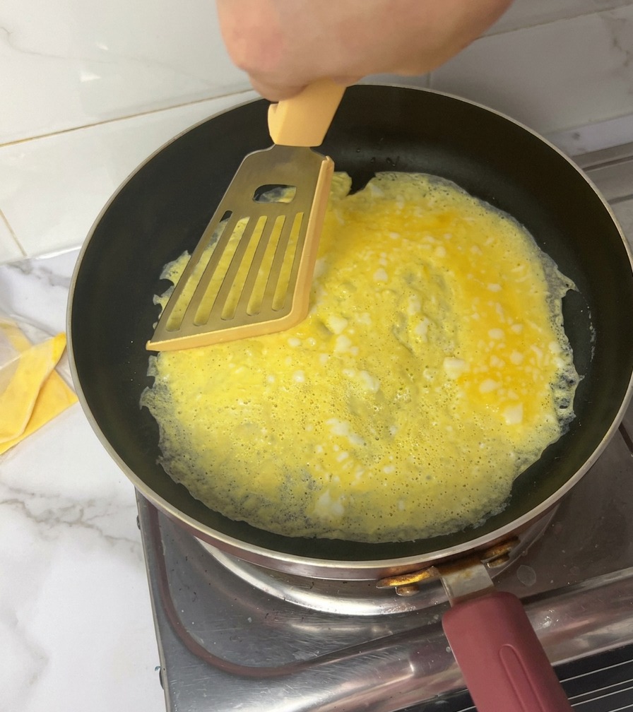 Una mano usando una espátula amarilla para cortar una fina tortilla amarilla en cuatro secciones dentro de una sartén negra.