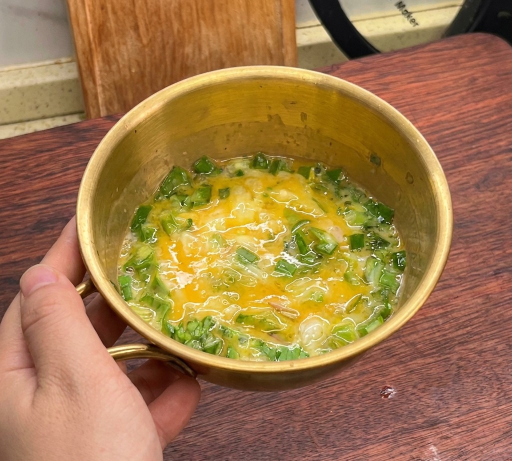 Mezcla de huevos batidos y lechuga combinados en un bol dorado.