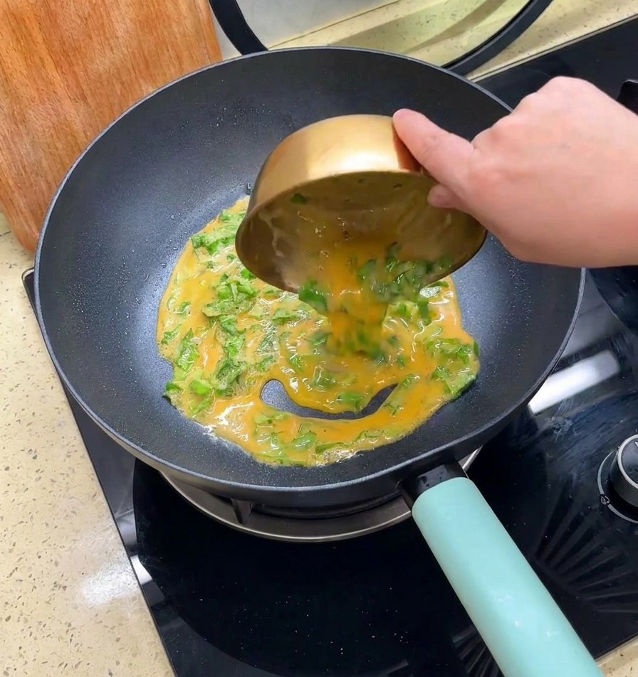 Mezcla de huevo batido y lechuga vertiéndose desde un bol dorado a una sartén negra.