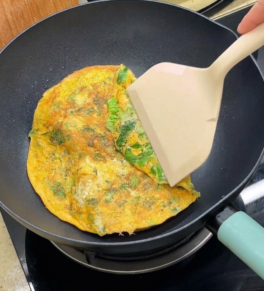 Una espátula doblando los bordes de la tortilla circular sobre las dos mitades del pan en la sartén.