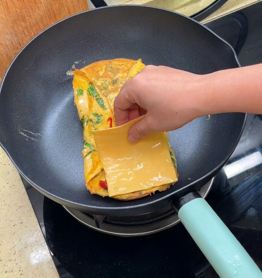 Una mano colocando una loncha cuadrada de queso amarillo sobre la tortilla plegada.
