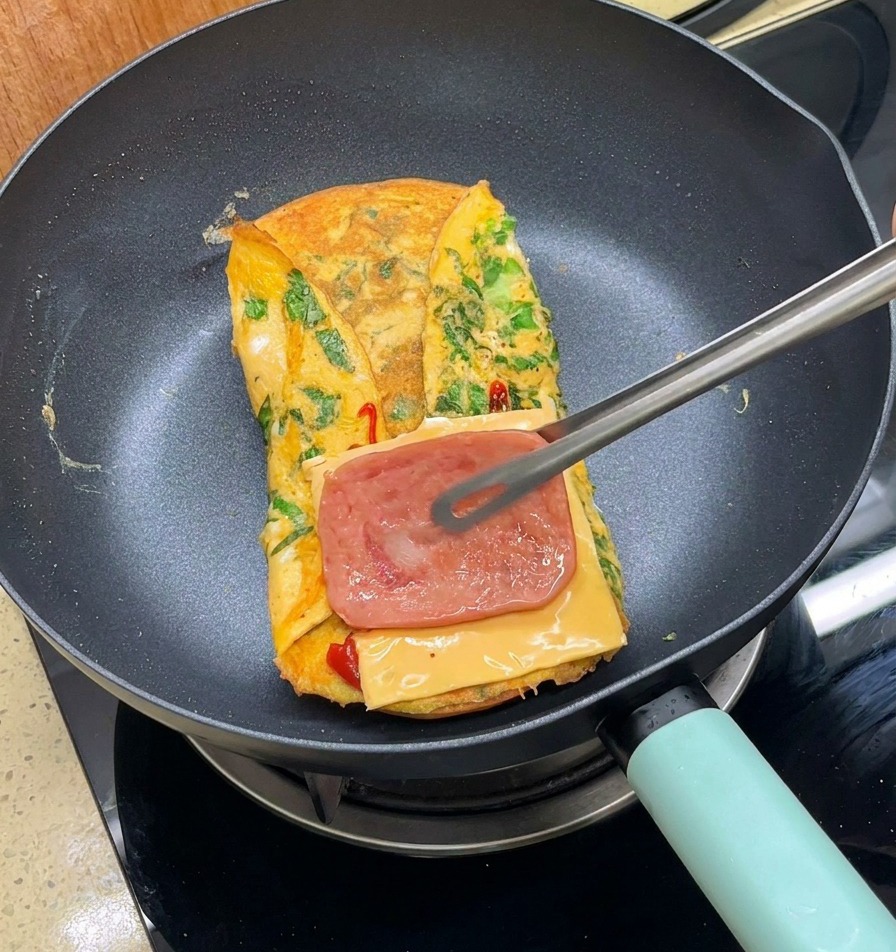 Pinzas metálicas colocando una tira de bacon cocinado sobre el queso en la sartén.