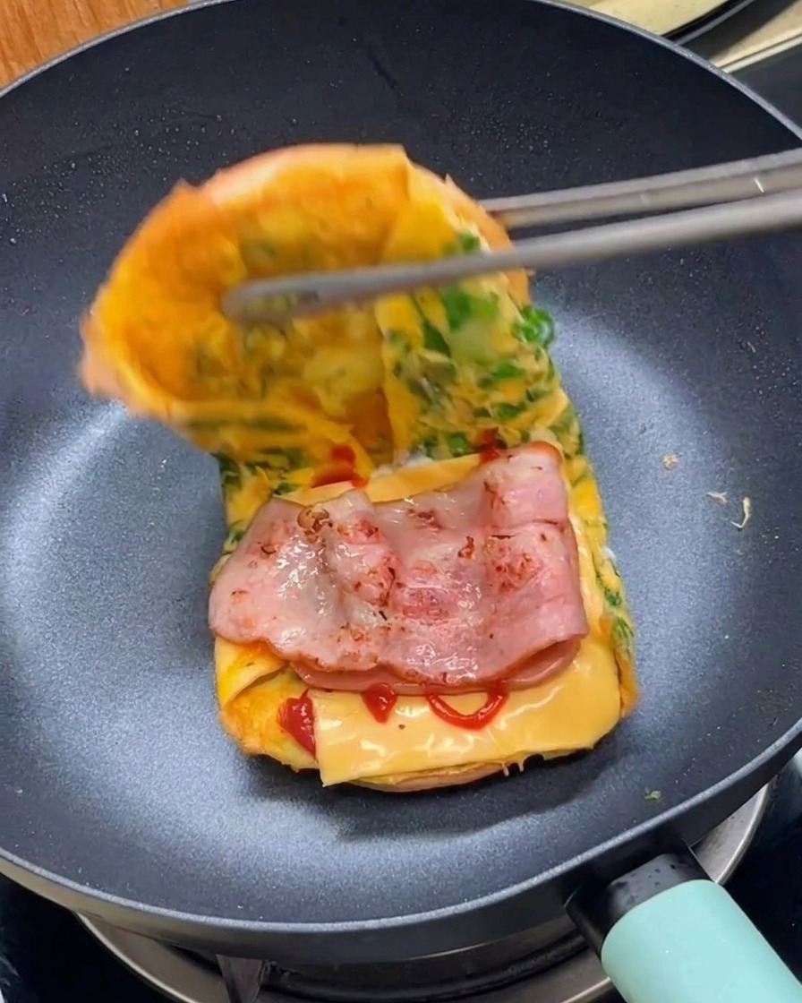 Pinzas doblando el conjunto para cerrar la hamburguesa de desayuno en la sartén.