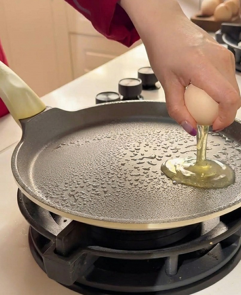 Dos huevos crudos siendo cascados sobre una sartén plana engrasada.
