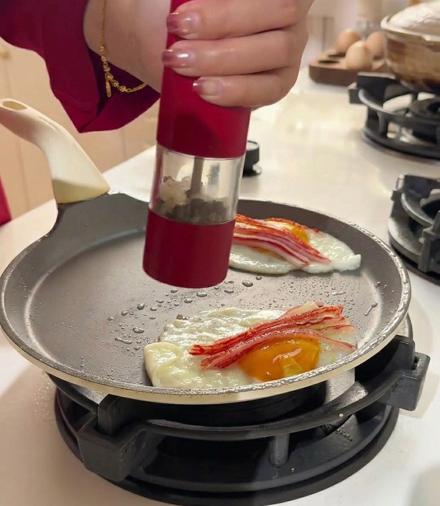 Un molinillo de pimienta sazonando los huevos y el cangrejo en la sartén.