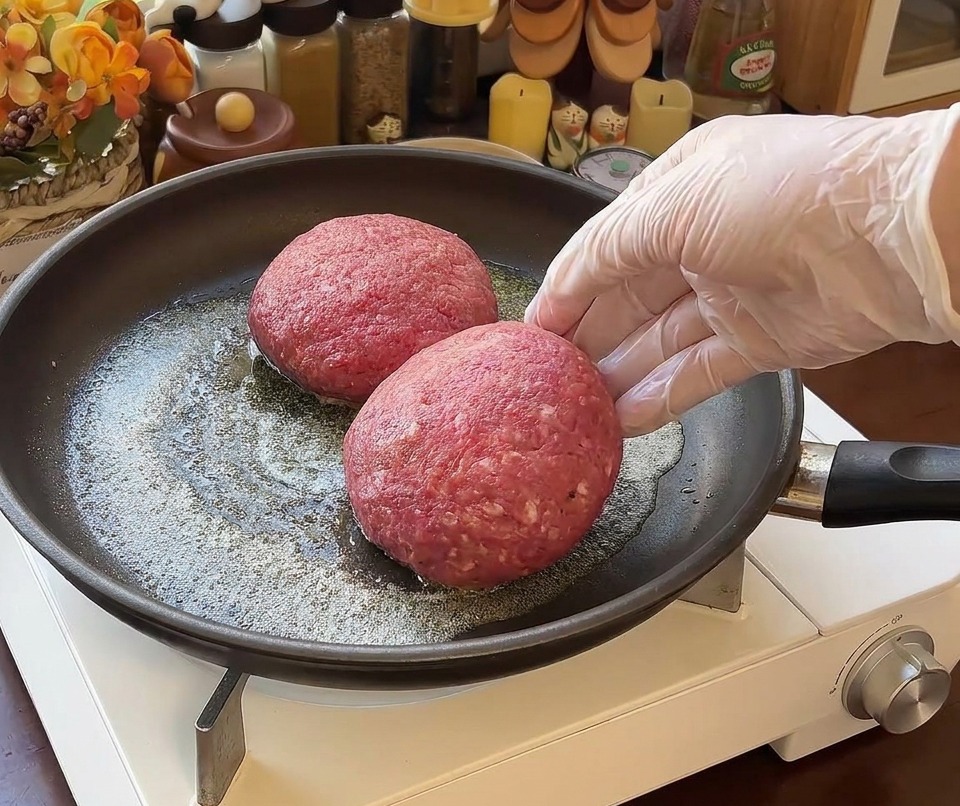 Dos porciones de carne rellenas en una sartén con mantequilla y una mano con guante al lado.