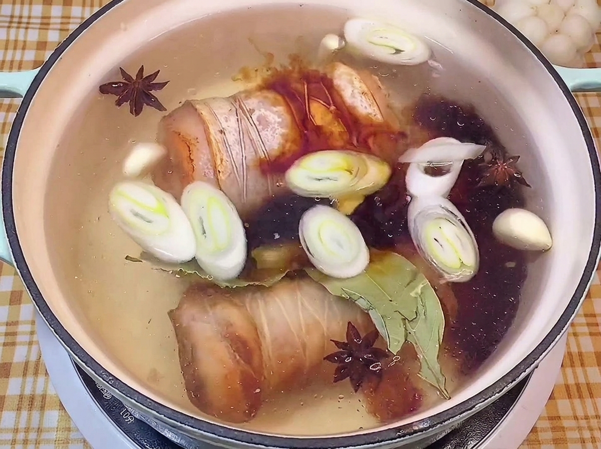 Añadiendo salsa de soja oscura a una olla con líquido de braseado, rollos de panceta y especias.