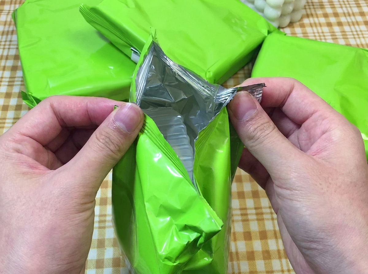 Dos manos abriendo un paquete verde de ramen instantáneo, mostrando la bandeja de plástico en su interior.