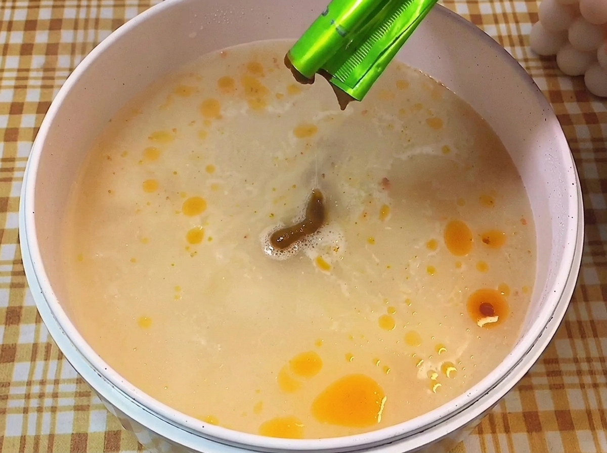Pasta de condimento marrón vertiéndose desde un sobre en una olla con caldo hirviendo y cremoso.