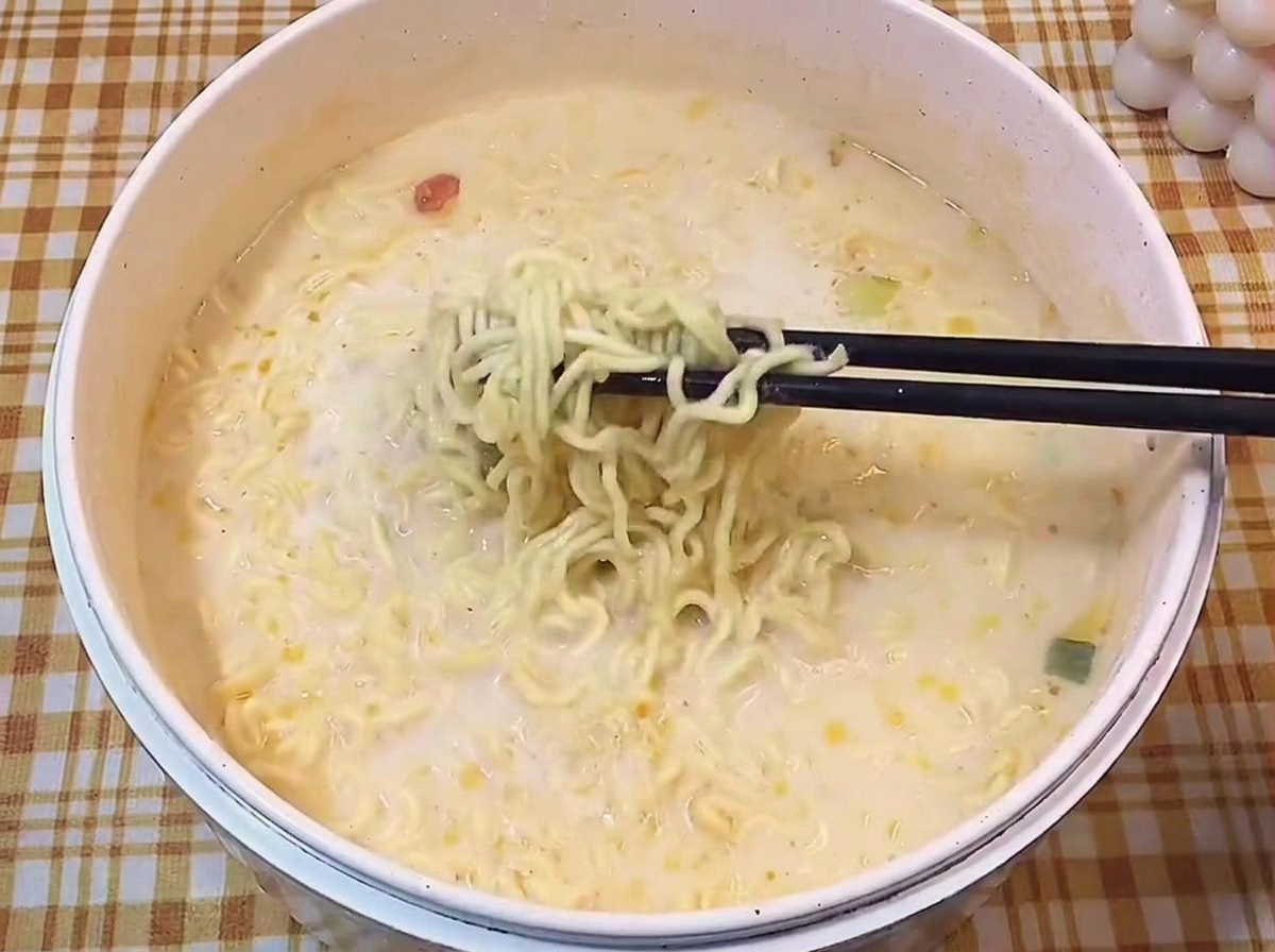 Palillos negros levantando una porción de fideos ramen rizados de un caldo blanco y cremoso.