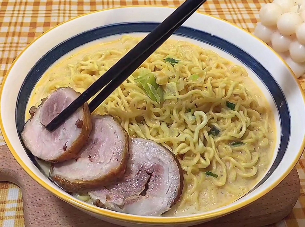 Palillos colocando con cuidado rodajas de panceta braseada en un tazón de ramen tonkotsu caliente.