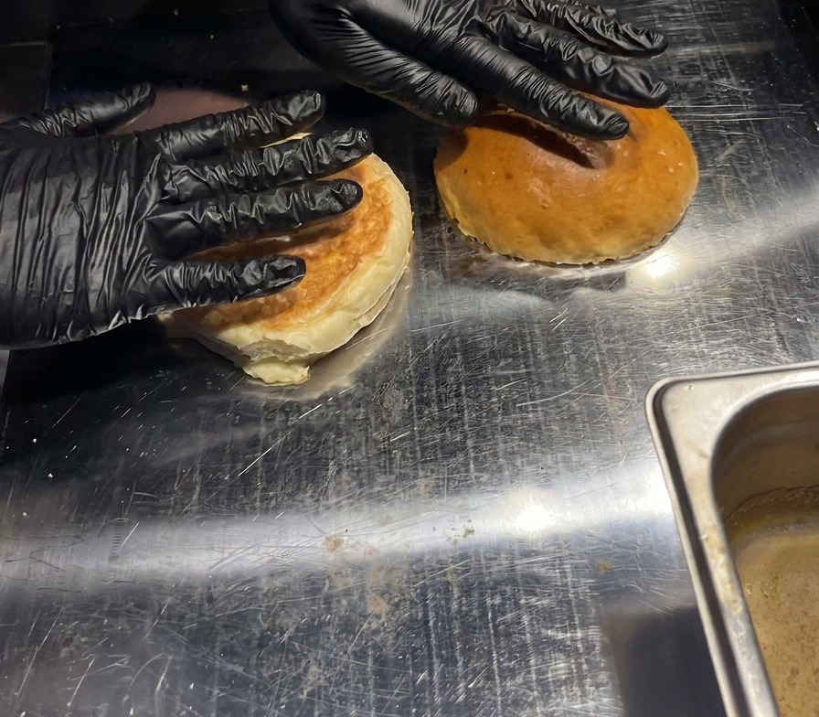 Dos panes de hamburguesa presionados con la mano sobre una plancha metálica caliente para tostar el interior.