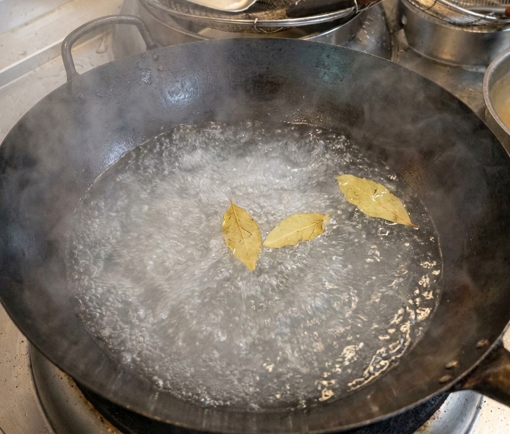 Un wok grande con agua hirviendo y tres hojas de laurel flotando en la superficie.
