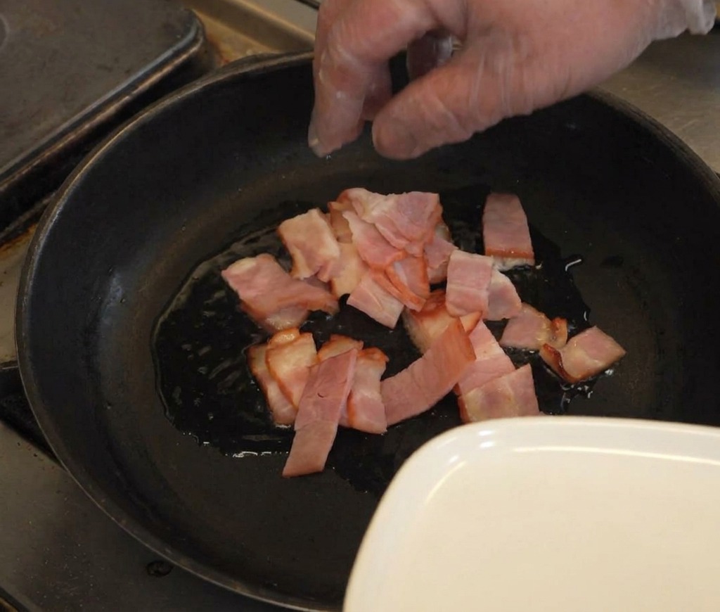 Bacón troceado en una sartén con una fina capa de aceite caliente.