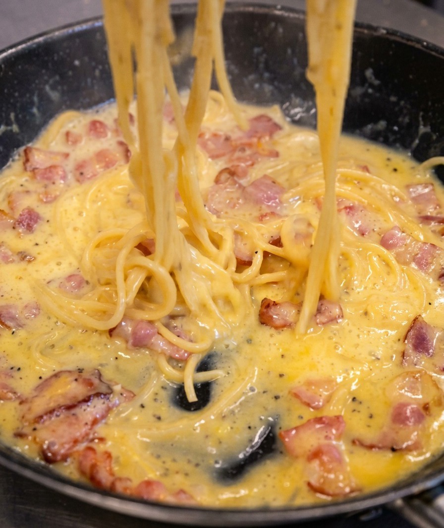 Espaguetis en una sartén mostrando una salsa que se transforma en una capa cremosa y amarillenta sobre la pasta.