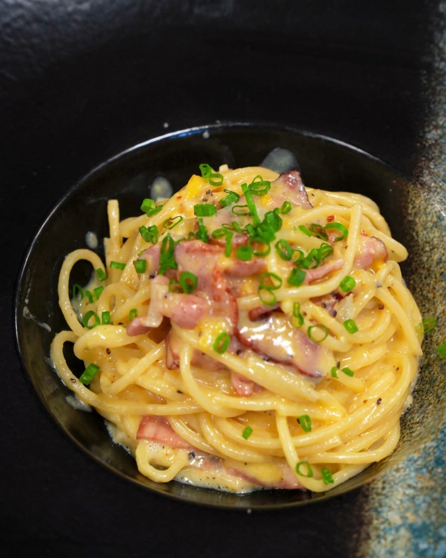 Ración de carbonara en un bol negro decorada con cebollino verde picado.