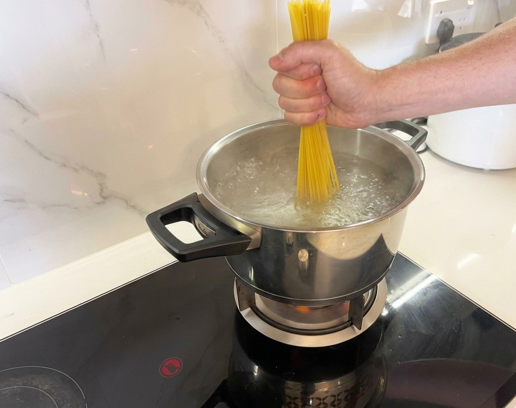 Una mano introduciendo un manojo de espaguetis secos en una olla de agua hirviendo.