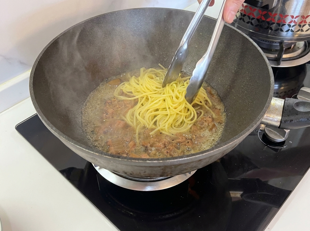 Pinzas levantando espaguetis cocidos directamente de la olla a la sartén con el guanciale.