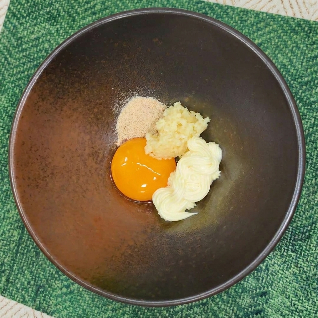 Polvo sazonador de fideos instantáneos añadido a un bol con yema, ajo y mayonesa.
