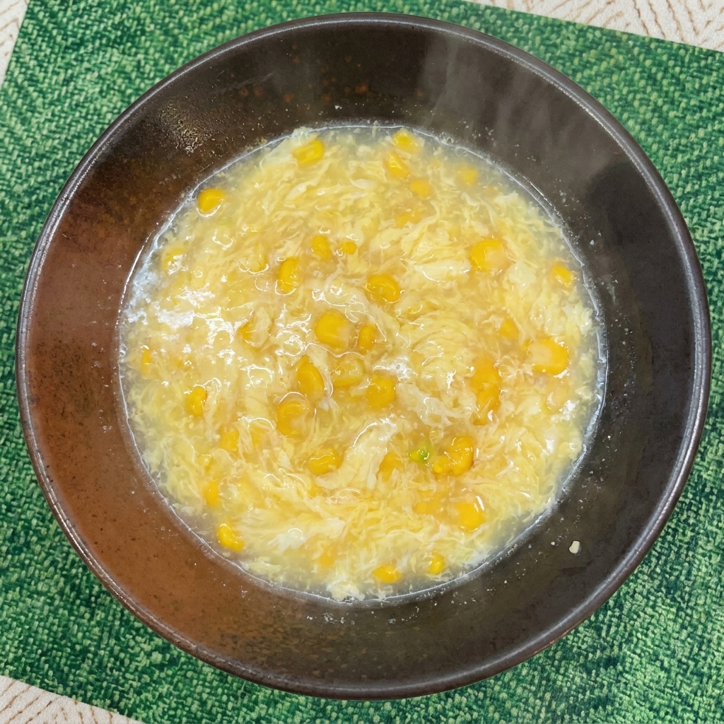 Un caldo de color amarillo claro mezclado con maíz dulce y trazas de huevo en un bol oscuro.