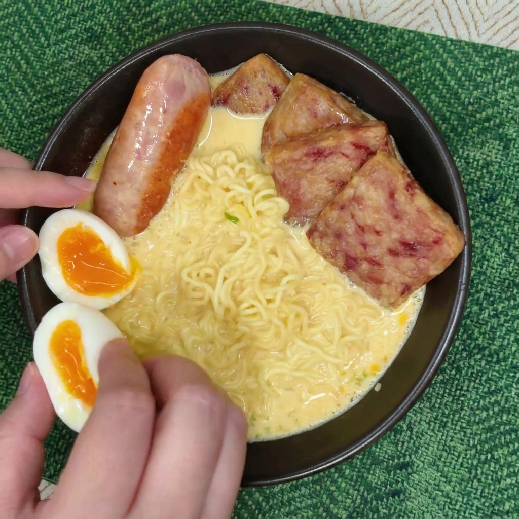 Manos colocando cuidadosamente dos mitades de un huevo pasado por agua con yema naranja brillante en un bol de ramen.