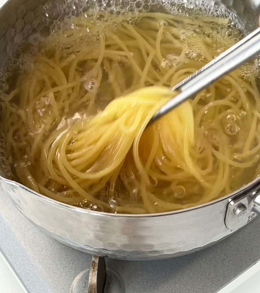 Espaguetis siendo levantados de una olla con agua hirviendo usando unas pinzas de metal.