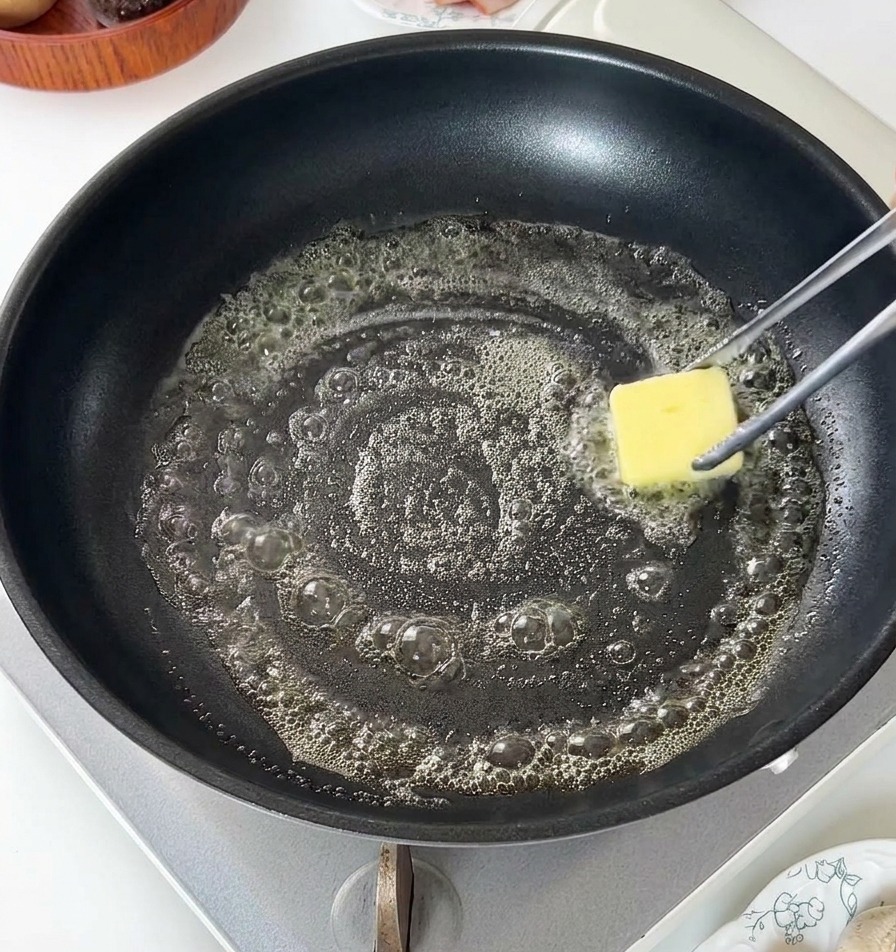 Un trozo de mantequilla amarilla derritiéndose y burbujeando en una sartén antiadherente negra.