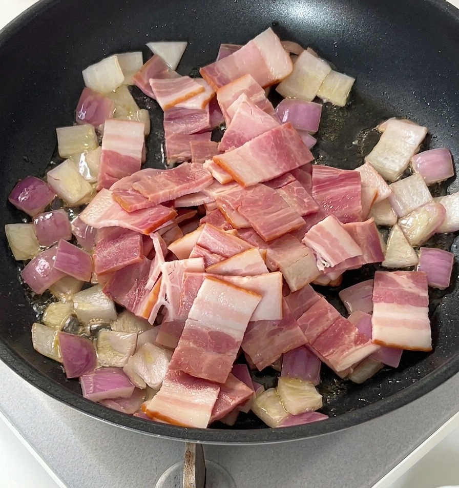 Trozos de bacon crudo sobre las cebollas salteadas en una sartén negra.
