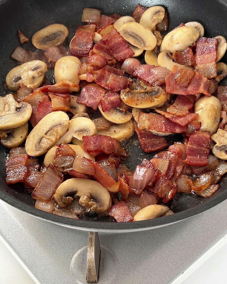 Sartén con bacon, cebolla y champiñones espolvoreados con pimienta negra.