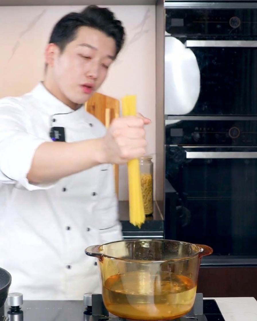 Un cocinero introduciendo espaguetis secos en una olla de cristal con agua hirviendo sobre el fuego.