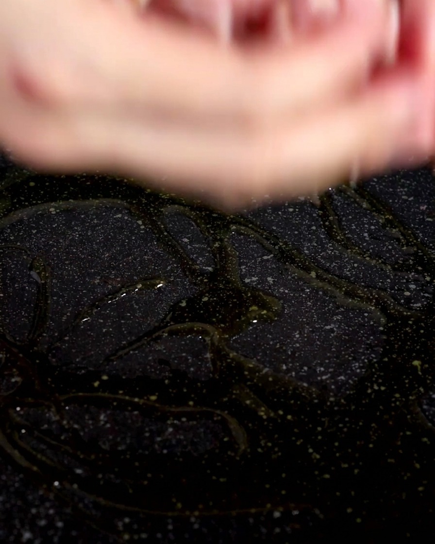 Primer plano de trozos de beicon cayendo en una sartén con aceite de oliva brillante.