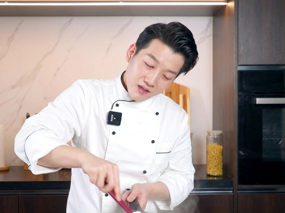 Cocinero removiendo la pasta cremosa con una espátula roja, integrando la salsa de huevo.