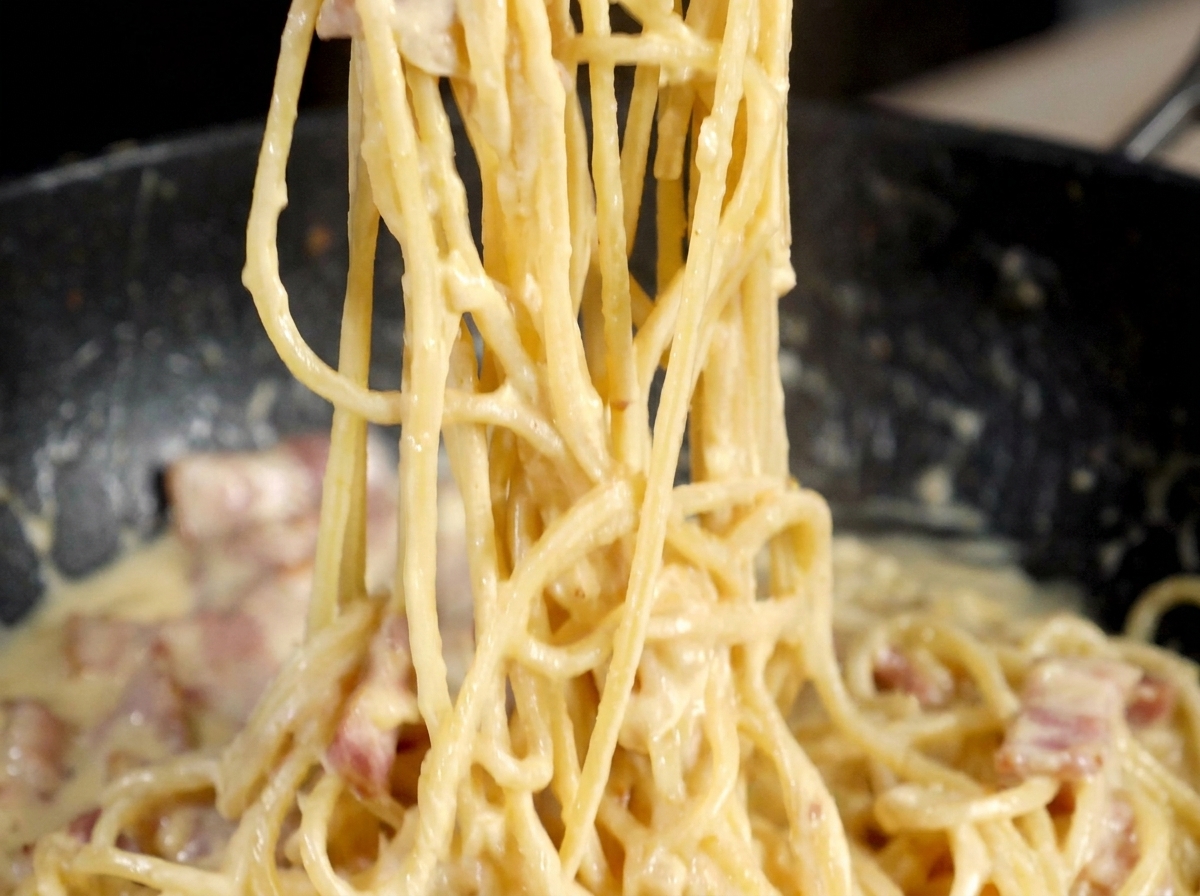 Un molinillo de metal moliendo pimienta negra sobre la sartén de pasta carbonara.