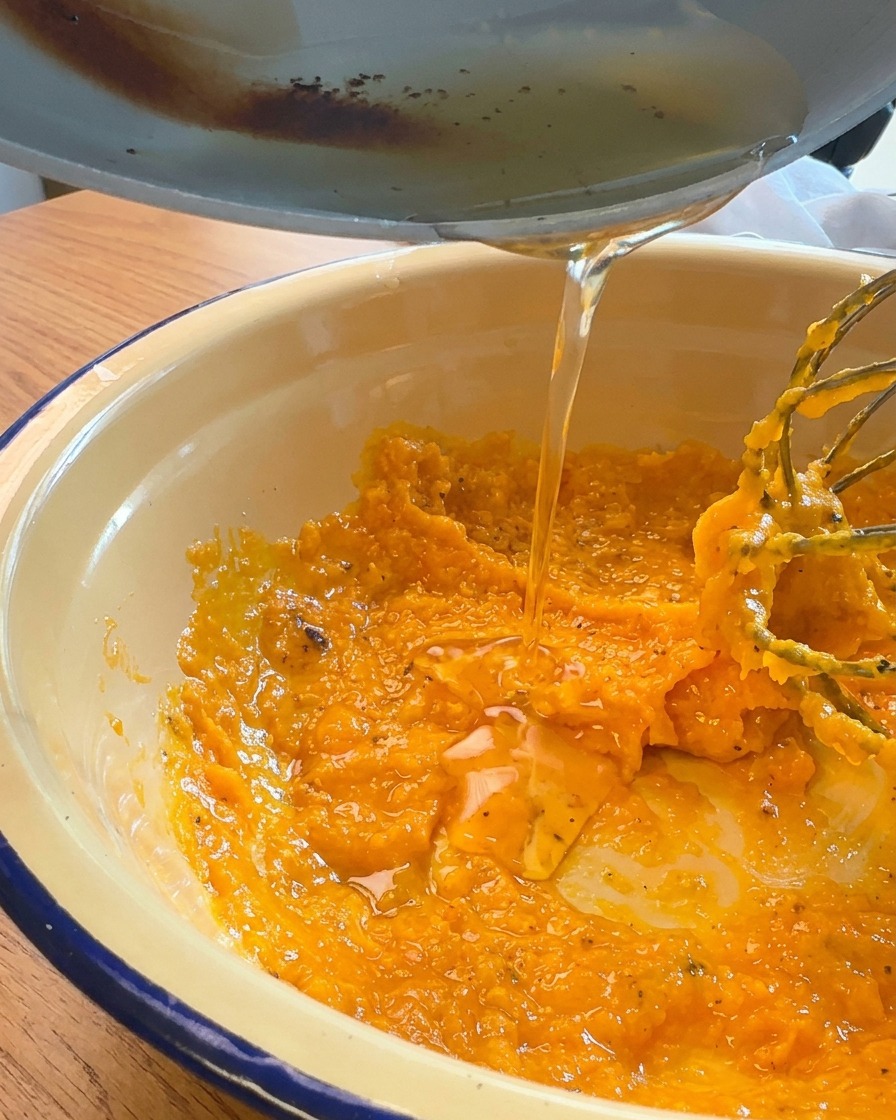 Grasa de cerdo líquida y dorada vertiéndose desde una sartén en un bol con una mezcla espesa de yema de huevo naranja y queso rallado.