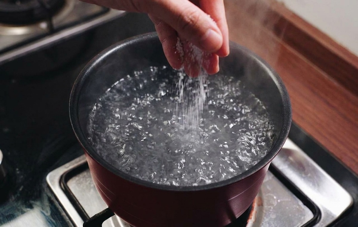 Una mano espolvoreando sal en una olla de agua hirviendo sobre una cocina.
