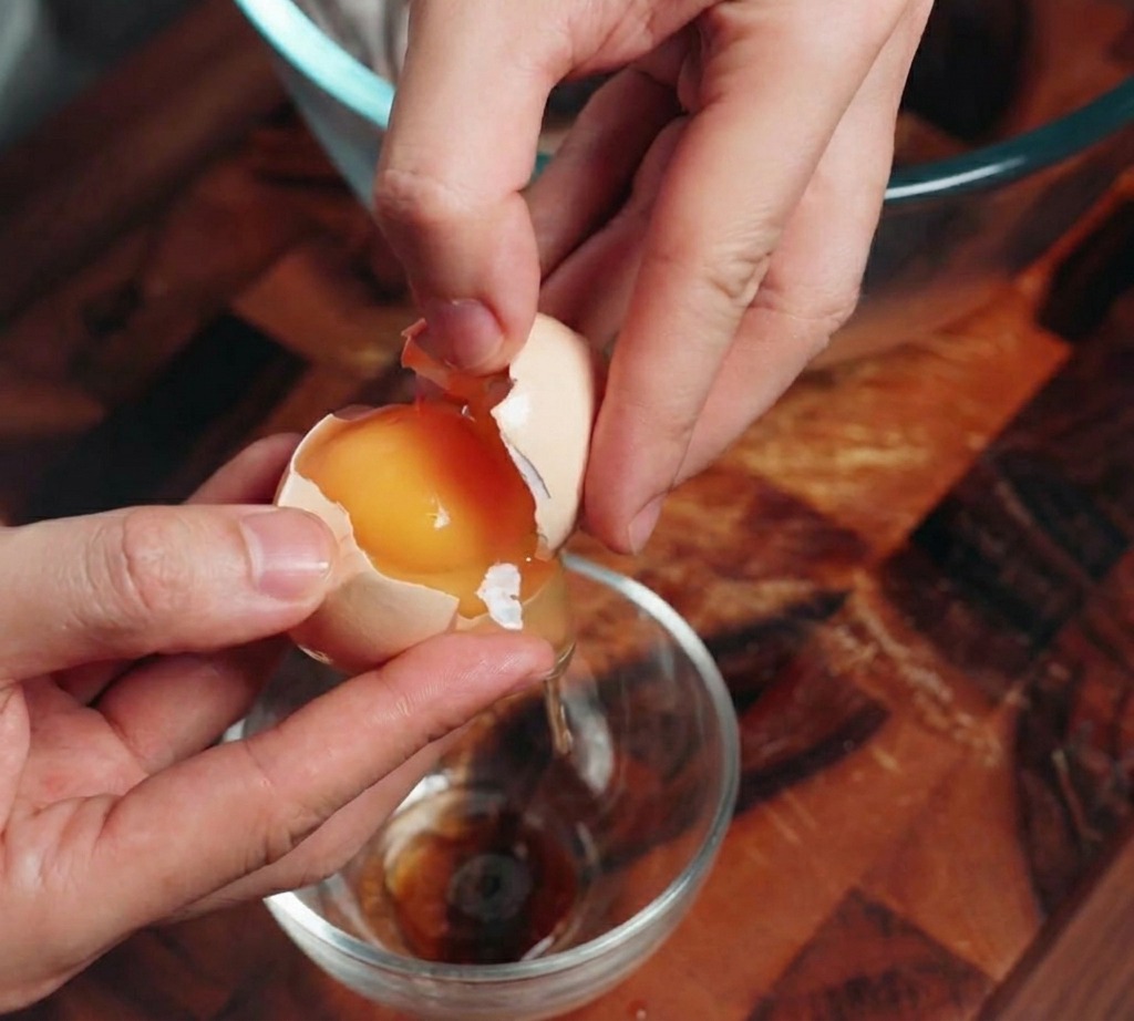 Primer plano de unas manos cascando un huevo y separando la yema naranja brillante de la clara transparente.