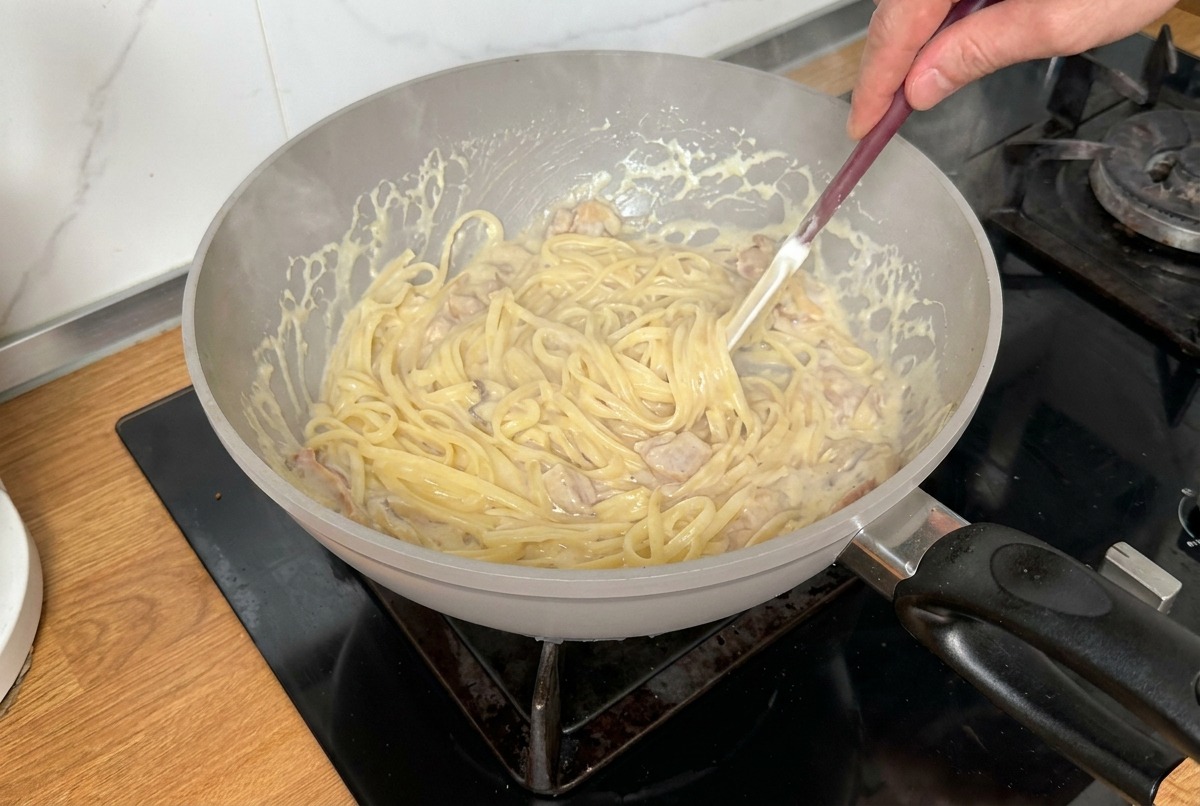 Pasta siendo mezclada con una espátula en una salsa cremosa para asegurar una cobertura uniforme.